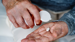 Elderly man pours a pill into his hand from a jar. Photo.